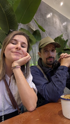 Multiracial couple with arabic man and caucasian woman taking selfie together at table, friends group laughing and enjoying chinese food lunch in indoor eatery, bonding and happiness moment