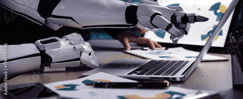 Wallpaper Mural A futuristic robot hand interacts with a laptop in a modern office setting, analyzing data and charts, showcasing the fusion of AI technology with business.Noogenesis Torontodigital.ca