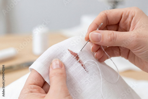 Hands stitching tear in white fabric with needle and thread