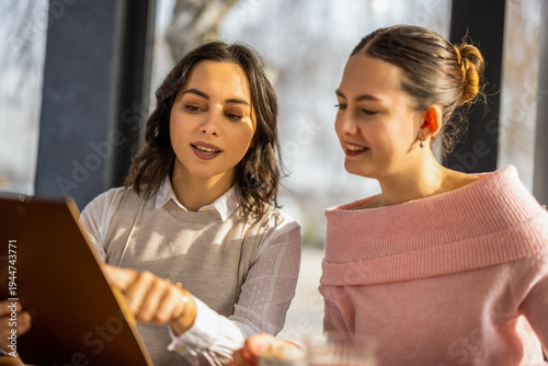 Φωτογραφία Two young diverse business women discussing documents and collaborating during a meeting in a cafe