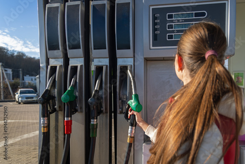 Woman refueling car at gas station pump. Close-up of a woman holding a fuel nozzle at a gas station pump, showing car refueling, transport costs, and everyday driving.
