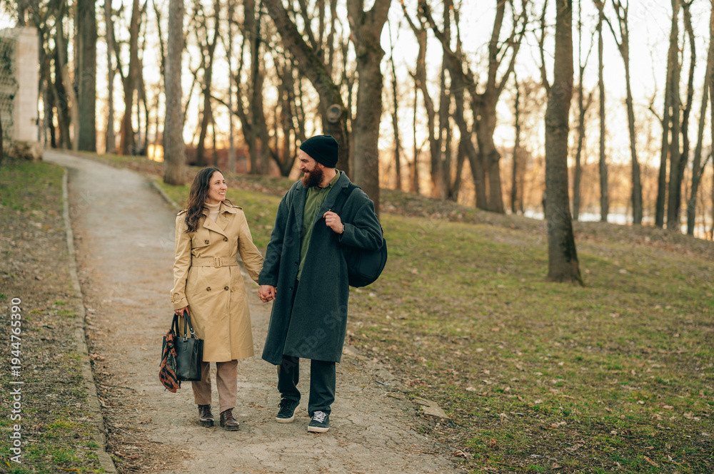 Fototapeta premium Couple Walking In Autumn Park Path, Two People Wearing Coats And Backpacks Sharing Conversation