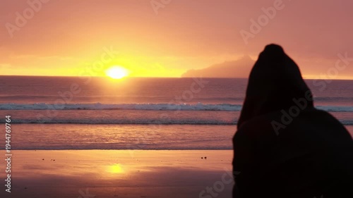 Silhouette of person watching sunrise over ocean with volcanic island near Anaura Bay, New Zealand