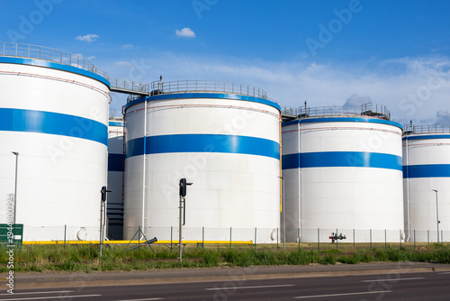 Row many large industrial fuel storage white tanks clear blue sky background on sunny day. Oil storage refinery depot liquid facilities. Energy hazmat railroad transportation storage and distribution