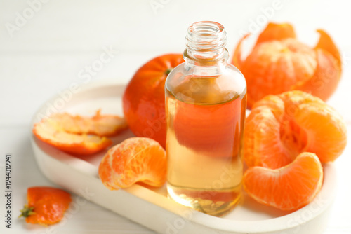 Bottle of tangerine essential oil and fruits on white table, closeup