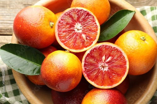 Whole, cut Sicilian oranges and green leaves in bowl on wooden table, top view