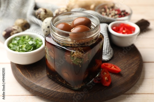 Photos Tasty pickled quail eggs in glass jar and ingredients on light wooden table, clo