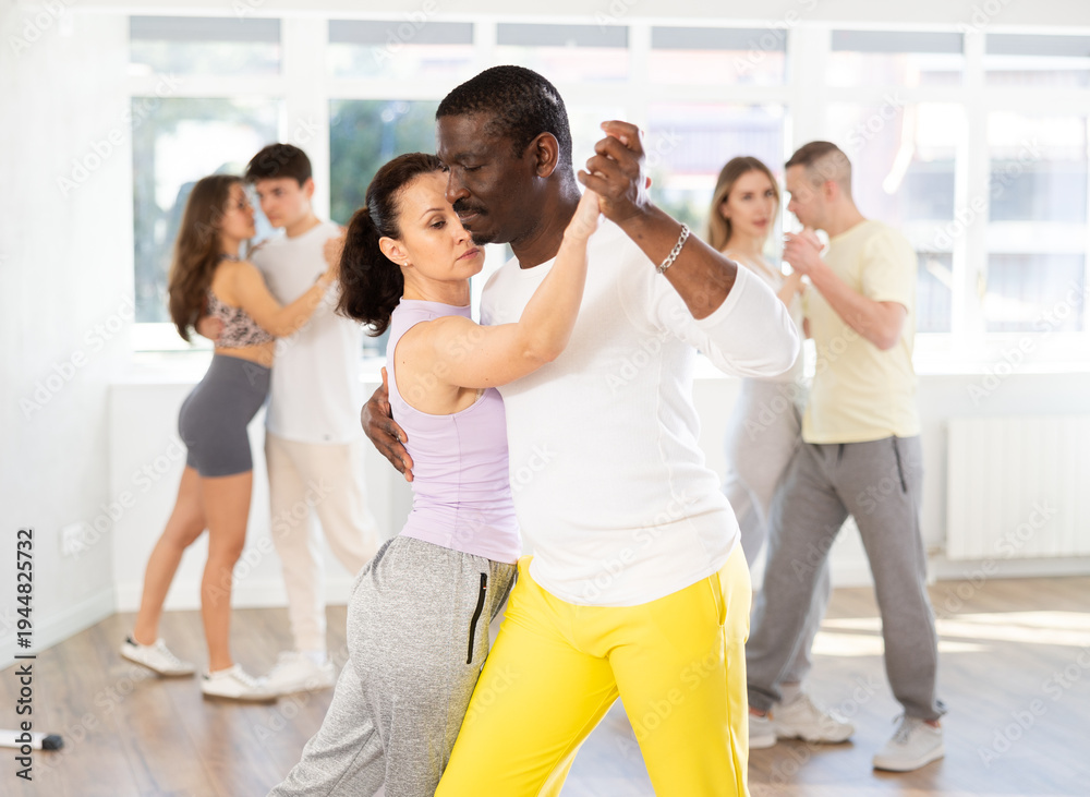 Fototapeta premium During rehearsal of reporting concert, woman with African-American man participants of dance workshop perform figure waltz. Group training and rehearsal, preparation for competitions