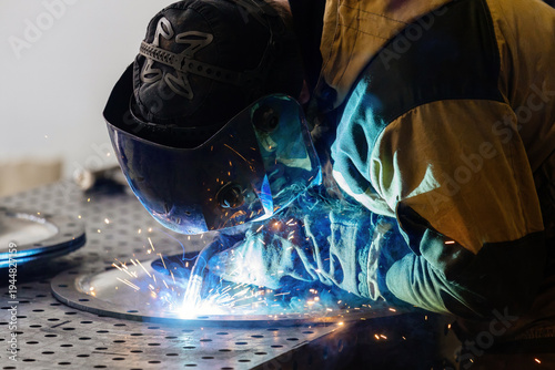Close-up shot of a welder in safety mask arc-welding steel parts