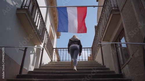 A woman walks up a staircase between two buildings with a flag hanging overhead