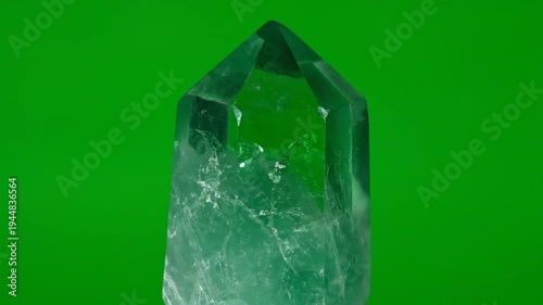 A close-up photograph of a green crystal with a pointed tip against a green background