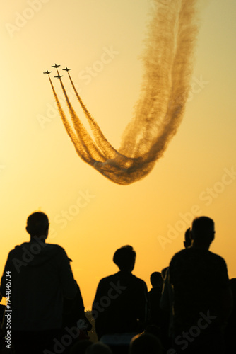 Aerobatic planes leaving smoke trails above spectators at sunset