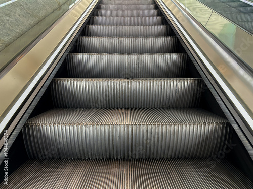 Close-up perspective of metal escalator steps moving upward inside a modern building.