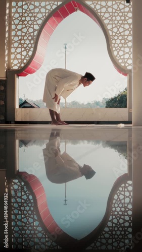A Muslim man performing Islamic pray inside a mosque during Ramadan, a peaceful spiritual moment with beautiful mosque architecture and reflection on the polished floor.