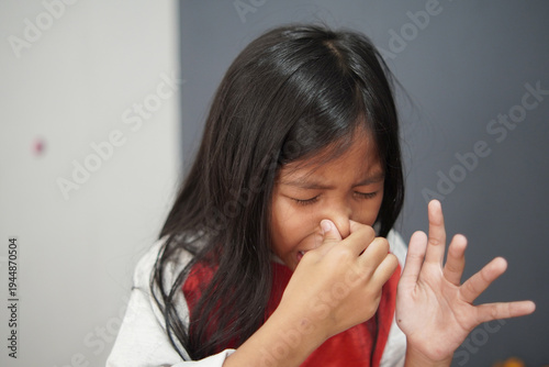 Disgusted little Asian girl pinching her nose due to bad smell, child reacting to unpleasant odor or stinky scent with funny expression, air pollution