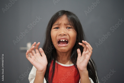 Hysterical little Asian girl crying and looking terrified, panicked child with fearful expression and defensive hand gesture, childhood trauma, bullying, and domestic fear