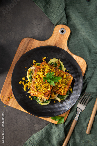 Top Down View of Roasted Tofu with Herb Crust and Sautéed Greens on a Black Plate