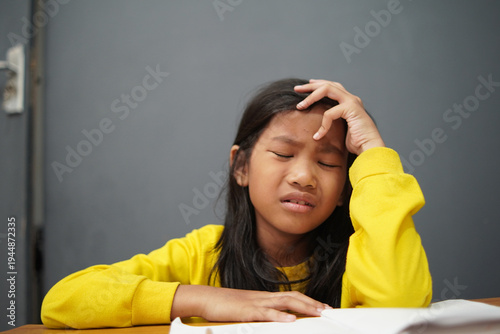 Stressed little Asian girl crying while studying, unhappy child having headache or difficulty with homework, academic pressure and learning disability