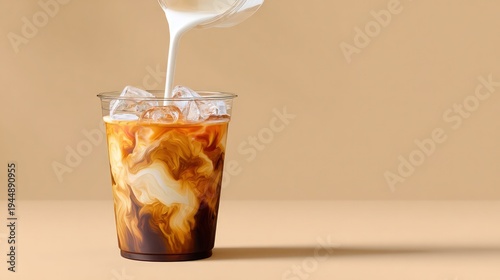 Milk streams into cup filled with ice and cold coffee, creating caramel and white liquid swirls, copy space