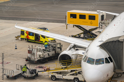 Foto Passenger aircraft parked on airport apron while ground crew operate service veh