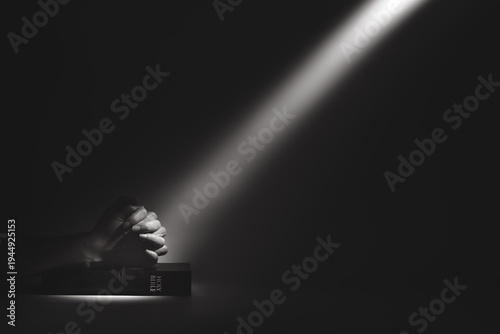 Εκτύπωση καμβά A strong beam of light illuminating a holy bible and the hands of a person praying, a background of faith and belief
