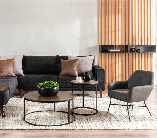 Contemporary living room with a plush black sectional sofa, round wood-and-metal coffee tables, mix of leather and fabric throw pillows, and a slatted wood accent wall in a trendy, modern style.
