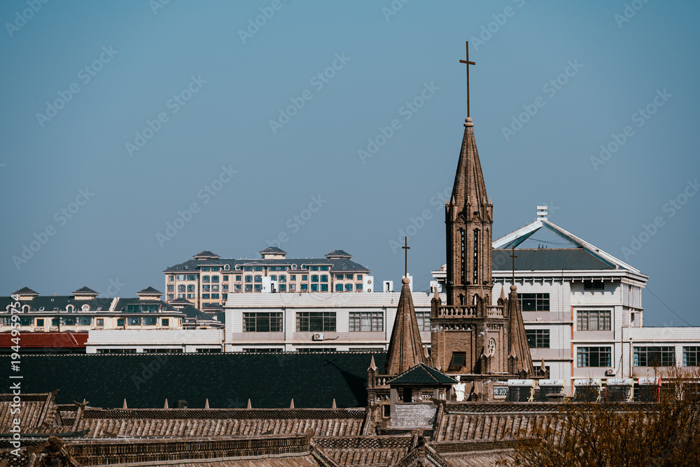 Obraz premium A distant perspective of the Catholic Church nestled within Qingzhou Ancient City. The church stands gracefully amid traditional Chinese architecture, showcasing a blend of Eastern & Western cultures.