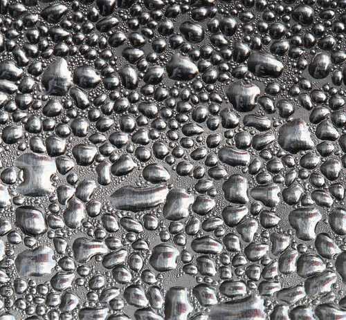Macro view of water droplets and condensation forming a textured moisture pattern on a reflective metallic or glass surface, creating an abstract background with natural liquid shapes