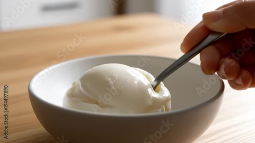 Spoon lifting a scoop of vanilla ice cream in a white bowl on a wooden table, warm natural light creates a cozy dessert moment, simple home kitchen feel