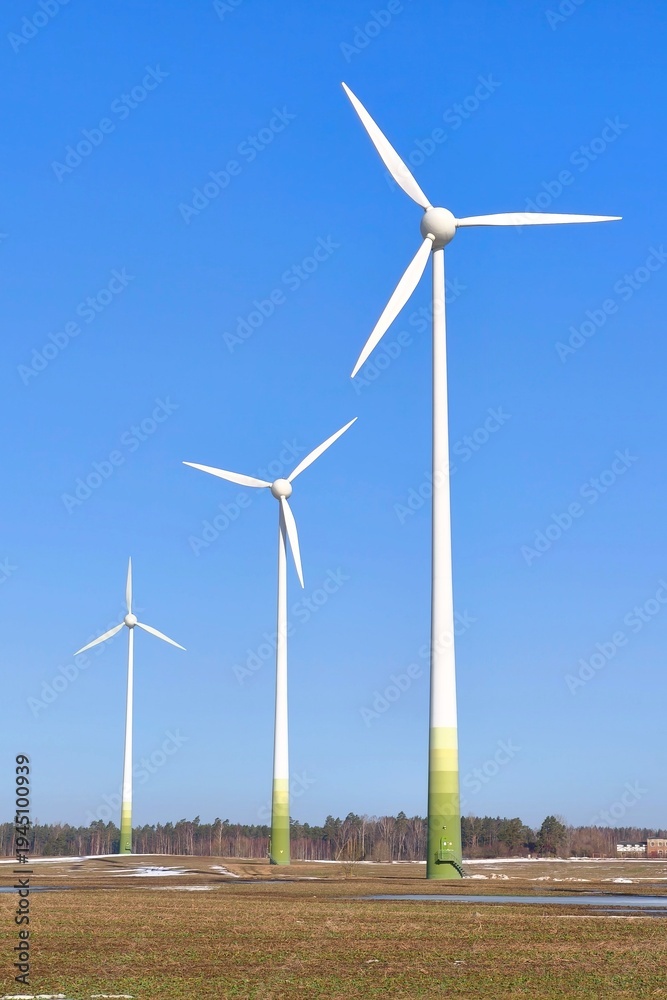 Fototapeta premium Wind turbines turning beneath a bright blue sky on a sunny day. Renewable energy technology producing clean electricity in a calm open landscape.