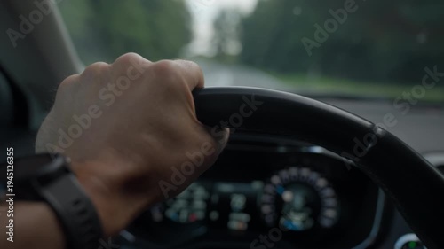 Man driving car through road in forest. Close-up of driver hand with wristwatch holding steering wheel with road and trees ahead. Concept of driving, transportation and road trip