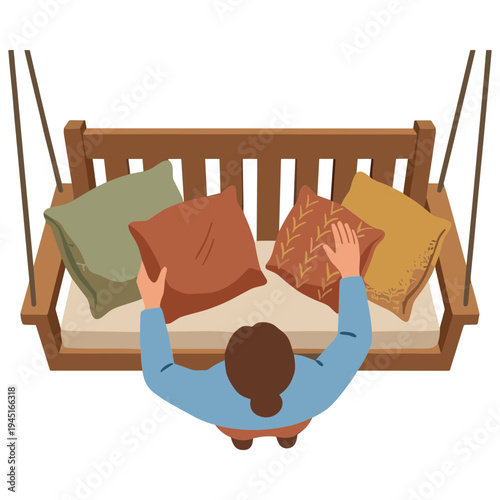 A person is arranging pillows on a wooden porch swing from an aerial view.