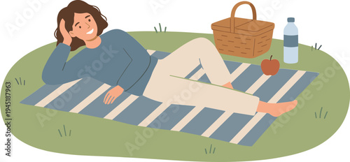 Woman lying on a picnic blanket outdoors with a basket and bottle