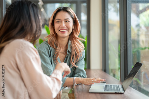 Pretty asian woman talking to friend aside laptop while meetup for work or study at counter in cafe