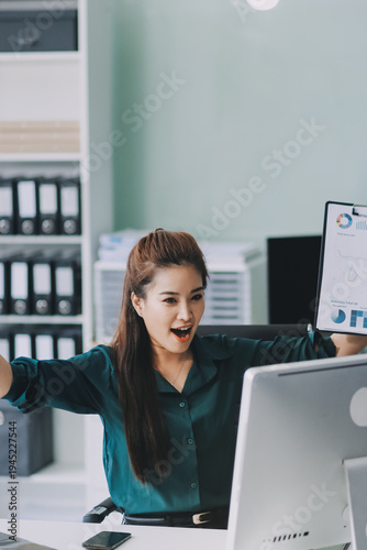 Determined asian businesswoman works late in a modern office, confidently analyzing data on her laptop, embodying success and professionalism with a smile