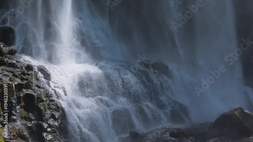 The majestic cascades of a flowing waterfall over rugged rocks, creating a dramatic and serene scene. The water cascades down with a lot of force