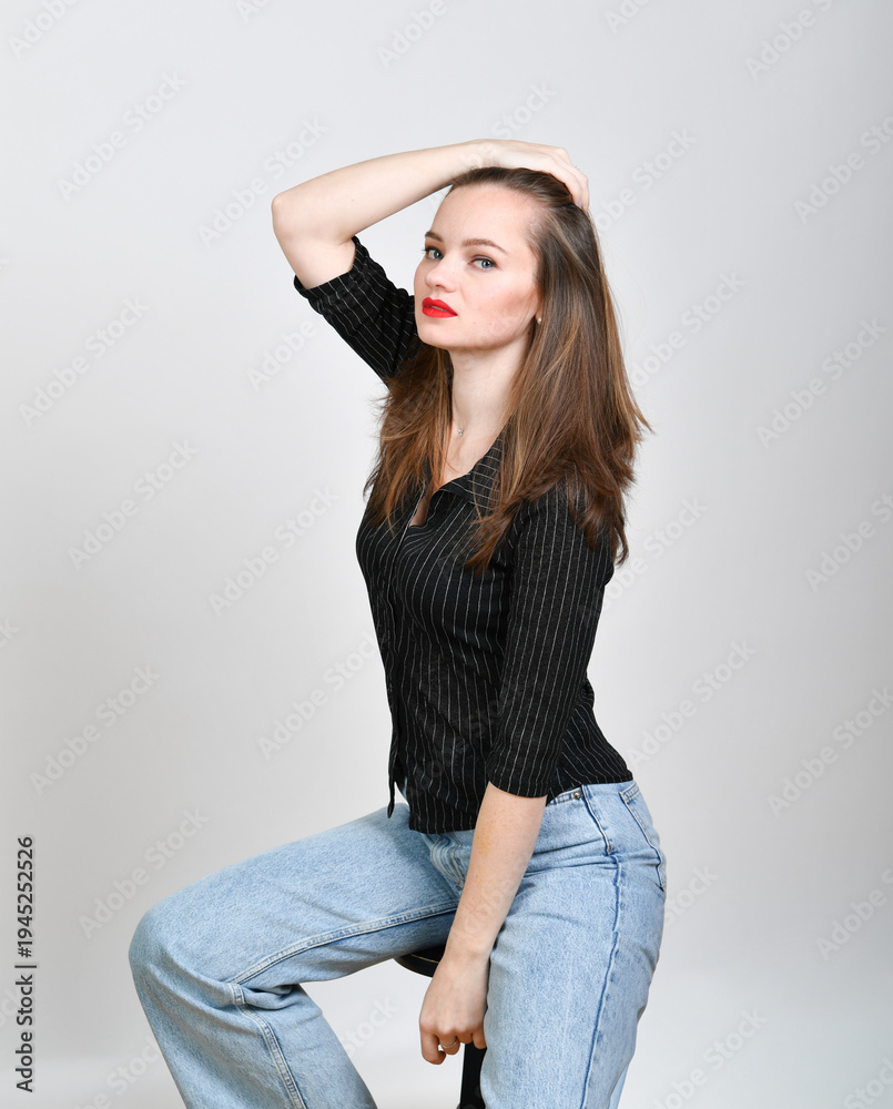 Fototapeta premium Selbstbewusstes Model posiert im Studio mit rotem Lippenstift und Jeans. Modernes Fashion-Porträt mit natürlichem Stil, Konzept für Mode, Lifestyle, Persönlichkeit und Stilbewusstsein.