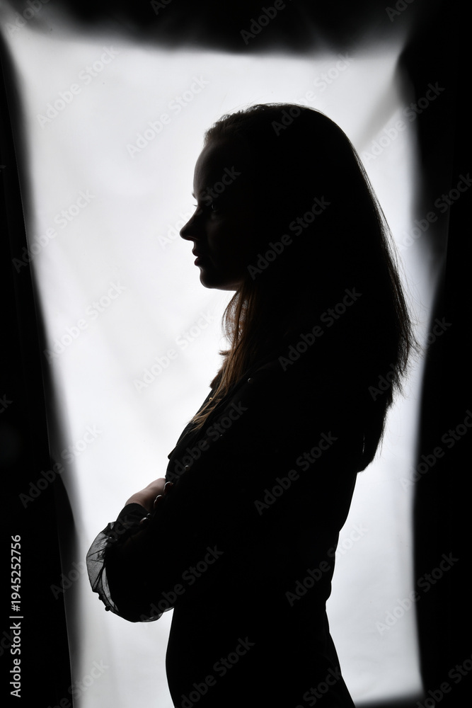 Naklejka premium Silhouette einer Frau im Gegenlicht mit verschränkten Armen. Künstlerisches Porträt mit klarer Kontur und dramatischem Licht, Konzept für Persönlichkeit, Stärke, Nachdenklichkeit und ästhetische Fotog