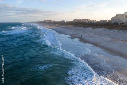 Aerial view of foamy waves crashing on the sandy beach of Amelia Island under a bright sky, Amelia Island, Florida, United States.