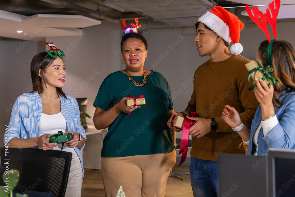 Obraz premium Diverse coworkers exchanging wrapped gifts while wearing festive headwear near desks and monitors