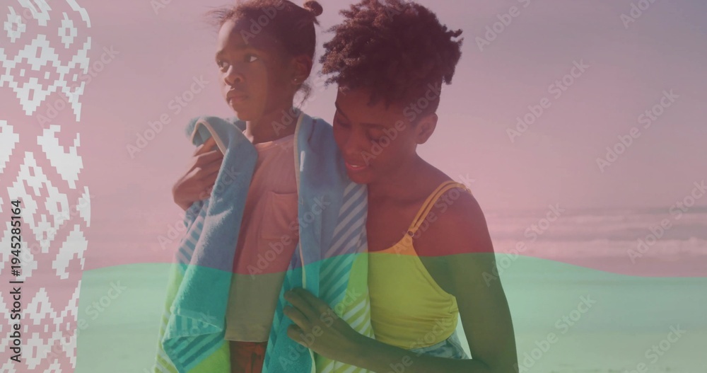 Obraz premium Wrapping mother in yellow tank draping turquoise-striped towel around daughter on sand, panel left