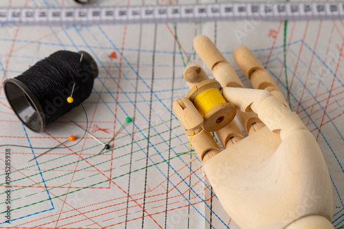 Fotografía Wooden hand resting on pattern and holding yellow thread, symbol of slow fashion