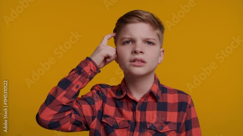 Boy Taps His Temple with Finger as Think First on Yellow Background