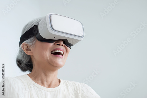 Happy senior Asian woman wearing VR headset experiencing virtual reality, active elderly lifestyle with modern technology at home