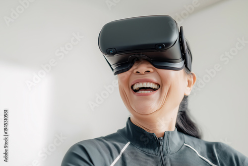 Happy senior Asian woman wearing VR headset experiencing virtual reality, active elderly lifestyle with modern technology at home