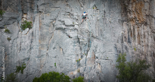 Foto Focused female lead climber moves up a towering limestone face, clipped into a rope for safety