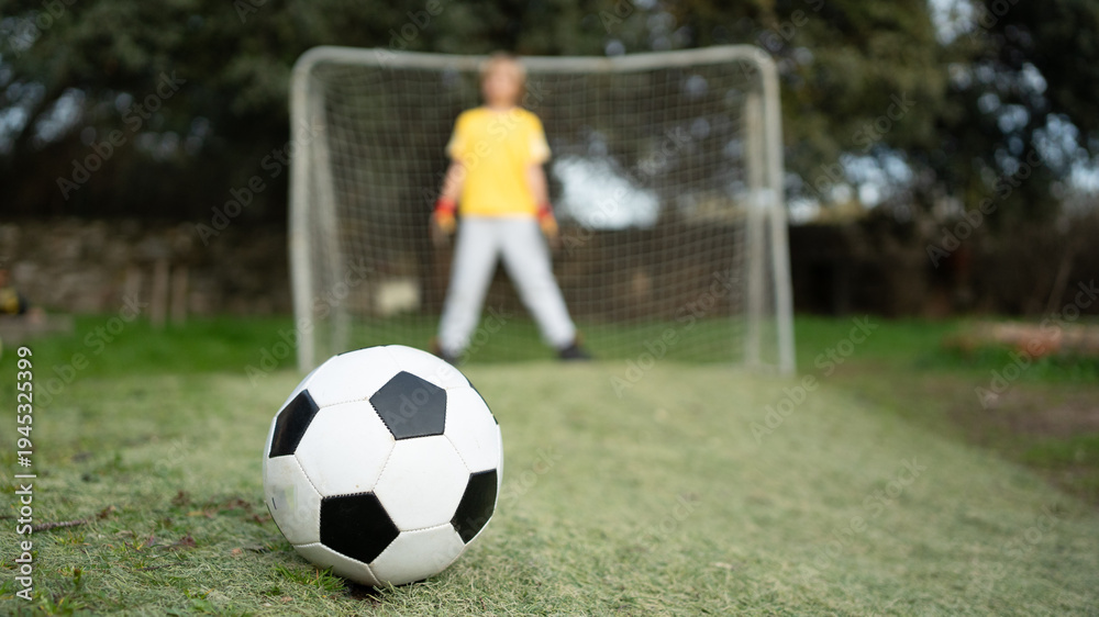 Obraz premium Soccer ball on grass with kid preparing to defend goal