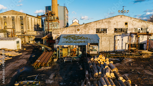 Aerial view of weathered industrial buildings stand in stark contrast to the neatly stacked logs, hinting at a blend of decay and industry, Sremska Mitrovica, Vojvodina, Serbia.