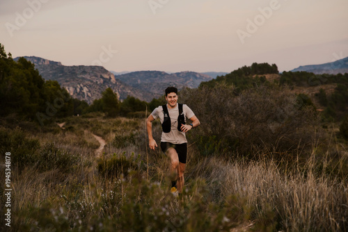 Male endurance runner running along a narrow mountain trail surrounded by natural vegetation. Outdoor sports concept focused on trail running, adventure and fitness.