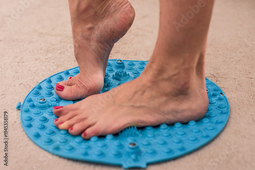 Closeup photo of young woman standing on massage mat doing feet gymnastics. Bare feet on acupressure mat for balance, massage, and foot arch support training